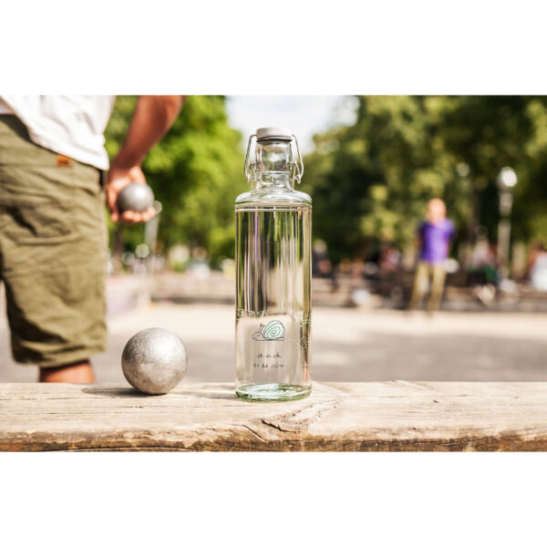 Soulbottle ok to be slow (1 Liter) Glasflasche Frontansicht auf einer Bank stehend beim Boule Spiel